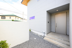 モダンなデザインの玄関エントランス。シンプルな色調の外壁が、落ち着いた印象を与えている。ポーチへのアプローチは石材で統一され、清潔感を感じさせる。