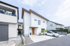 家の前面に広がる駐車スペースと、清潔感のある白い外観が特徴のモダンな住宅。