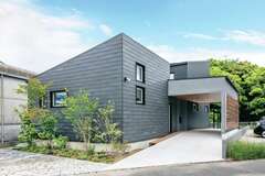 屋根付きのエントランスがある角張ったフォルムがクールな外観。濃いグレーのガルバリウム鋼板で外壁を統一し、ガレージの天井を板張りにしてアクセントをつけた【ainoa.life くらはし建築】