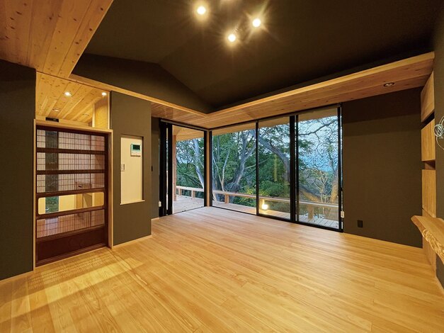 勾配天井とハイサッシを採用したことで、より広く感じるリビング。床は無垢のヒノキ、下がり天井と軒はスギ。格子戸の向こうはキッチン