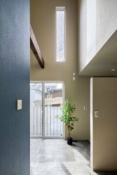 天井が高く開放的な玄関ホール。窓から差し込む自然光が空間を明るくし、植栽がアクセントを添えている。