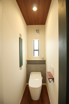 シンプルでモダンなトイレ空間。天井や壁にアクセントがあり、居心地の良い落ち着いた雰囲気を演出している。【小野田産業～designers house project～】