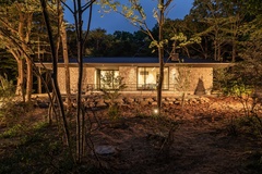 木々に囲まれた平屋の外観。夜のライトアップが建物の美しさを引き立て、自然と調和した落ち着いたデザインである。【栃木ハウス】