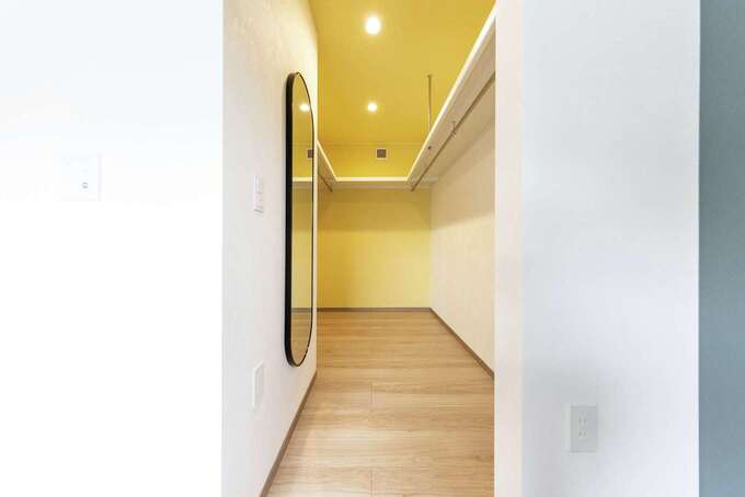 寝室のウォークインクローゼットは奥さまの好きなイエローのクロスで明るい雰囲気に。コの字型の収納スペースと壁に取り付けた鏡でショップのような空間に仕上げた