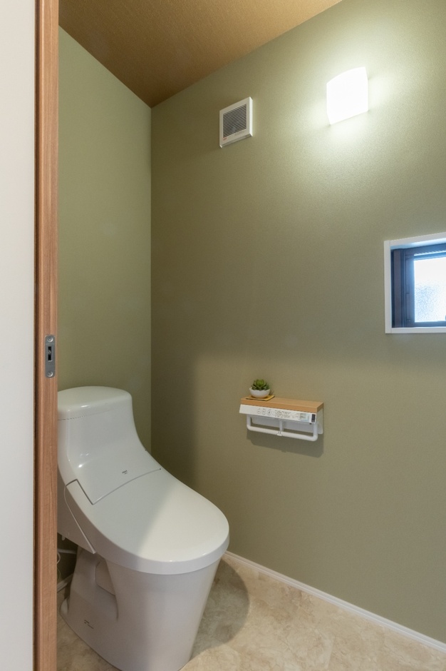落ち着いた色合いの壁紙を採用したシンプルなトイレ空間。小窓から自然光が入り、明るく清潔な印象を与えるデザイン。