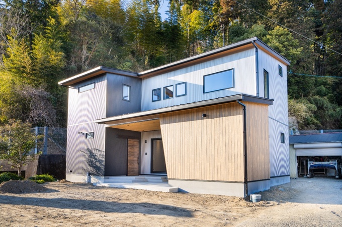 木目とガルバリウムが調和するモダンな二階建ての住宅。周囲の自然と美しく融合し、遊び心のある住環境を提供するデザインである。