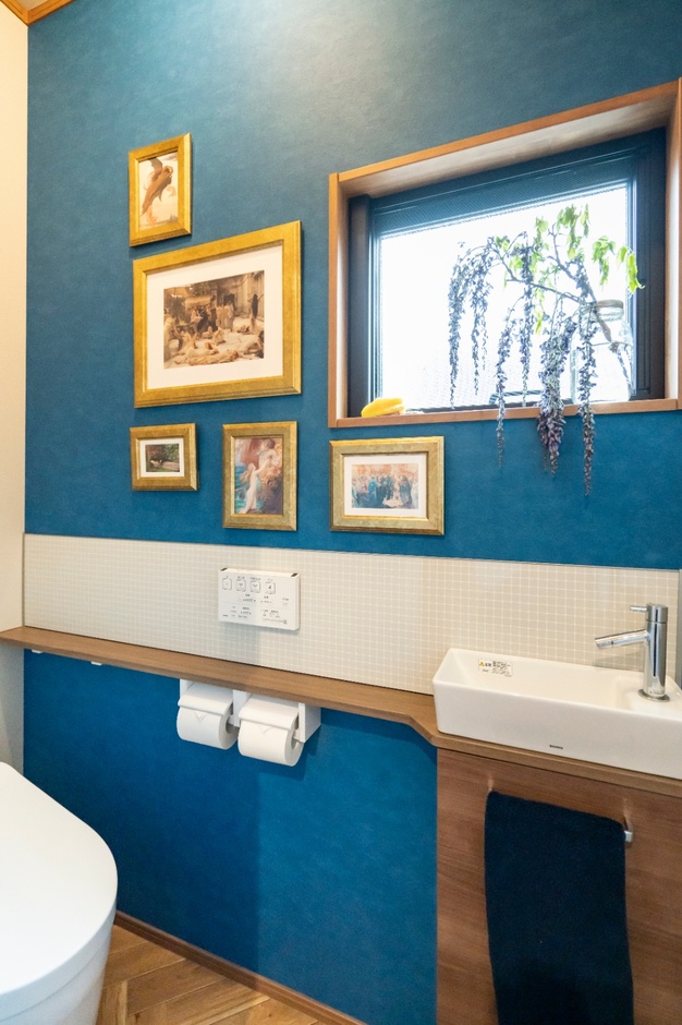 シックなブルーのクロスにブラウンのカウンターが調和し、洗練された印象のトイレ空間。壁に飾られたアートがアクセントとなり、さらに魅力を引き立てている。