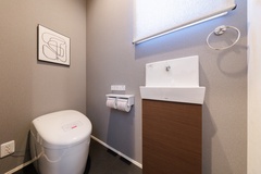 シンプルで洗練されたデザインのトイレ空間。機能的な手洗いボウルと壁掛けのアートがアクセントになっています。