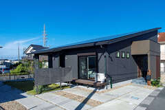 平屋のようにも見えるシンプルモダンな外観デザイン。片流れの屋根に30kWの大容量ソーラーを搭載している。フェンスの向こうにウッドデッキと庭もある【AQURA HOME（アキュラホーム）】