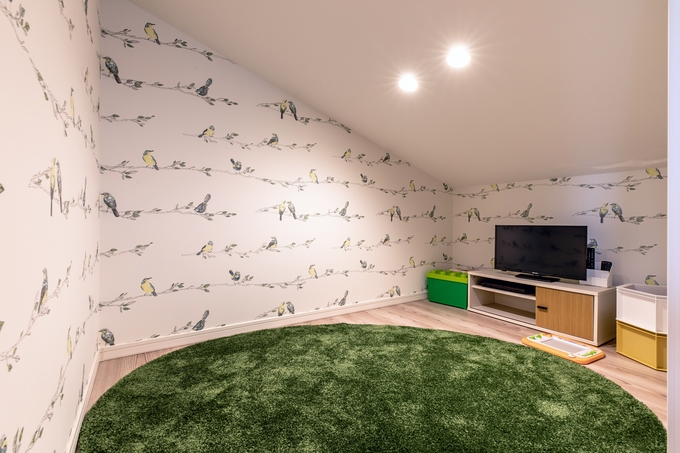 鳥のイラストが描かれた壁紙を使用した屋内遊び場。柔らかな円形カーペットが敷かれ、安全で楽しいスペースを提供している。