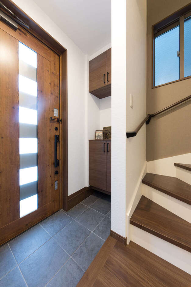 玄関はホールをなくしてスペースを節約。たたきの石板タイルが室内のヴィンテージインテリアと調和している。玄関ドアは採光ができるタイプにして閉塞感を軽減