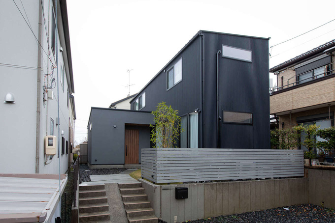 高低差を利用して建てたI邸。駐車場と階段は建築前のまま。両隣の建物が近いため、視線が合わないよう窓の大きさと位置に配慮した。屋根にソーラーパネルを搭載し、光熱費を抑えた低燃費な暮らしを実現