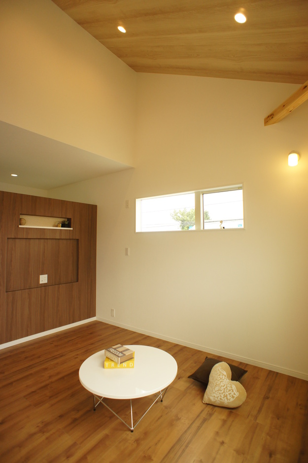高い天井と木目調のフローリングが魅力的な小屋裏収納。柔らかい光が差し込む窓があり、心地よい雰囲気を演出している。シンプルなデザインが落ち着きを感じさせる空間である。
