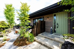 自然素材を活かした外壁が印象的な住居の外観。玄関アプローチには石畳と植木がバランスよく配置され、訪れる人を温かく迎える工夫が感じられます。