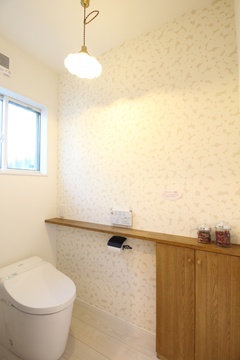 シンプルで清潔感のあるトイレ空間。アクセントクロスと木製キャビネットが温かみを加え、機能性とデザイン性を両立している。【小野田産業～designers house project～】