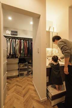 脱衣室と離したかった手洗いコーナーは、キッチンの手前に設置。娘さんが自分で手を洗えるよう練習中だ。奥はファミリークローゼット。ヘリンボーン柄のフローリングが高級感を演出する【三和建設】