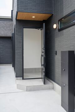 落ち着きのあるダークトーンの外壁に合わせたスタイリッシュな玄関ドア。シンプルなデザインでありながら現代的な印象を与える入口である。【K-rise】