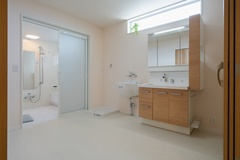 広々とした脱衣スペースには洗面台が設置され、清潔感あふれるデザイン。自然光が差し込む窓があり、明るく快適な空間である。