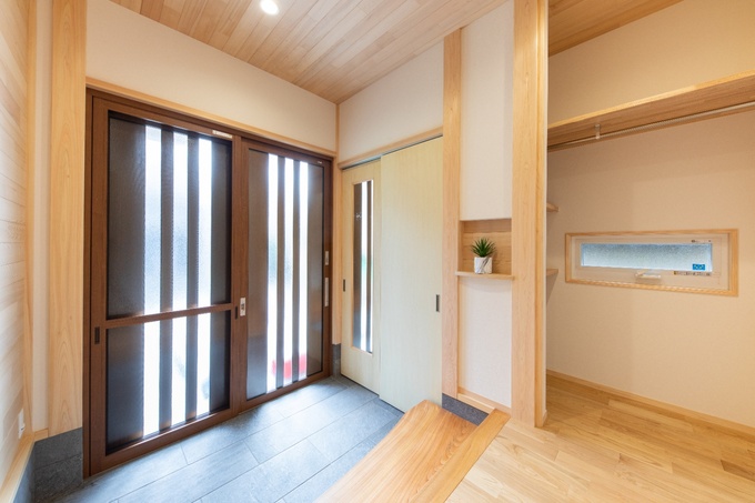 木の温もりが感じられる玄関ホール。明るい照明が雰囲気を和らげ、来客を温かく迎え入れる空間である。スッキリとしたデザインが印象的。