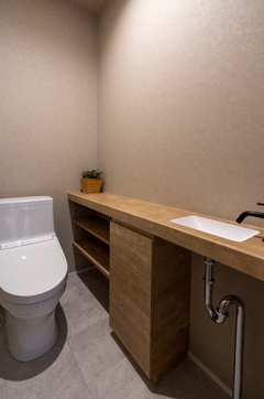 シンプルで洗練されたデザインのトイレ空間。造作の手洗いカウンターを設置し、収納スペースも充実している。【アールスタジオ】