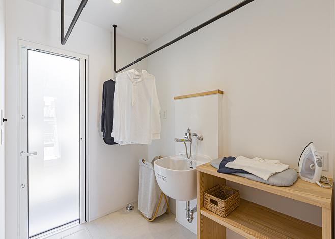玄関からすぐ行けるランドリーは、家事カウターと室内干し、スロップシンク付きで、洗濯物を洗う・干す・アイロンをかける・たたむという一連の作業が1か所でできる