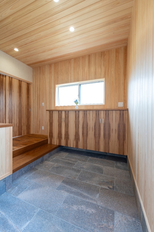狭小住宅だがあえて玄関土間は広くした。帰ってきて1番に入る場所だからこそ、ほっとする開放感のある空間づくりにこだわった。壁や天井は上質なヒノキ板張り。靴箱天板はサクラの1枚板、敷台はアサメラの1枚板を使用。気持ちにゆとりが生まれ訪問客を気持ちよく迎えられる