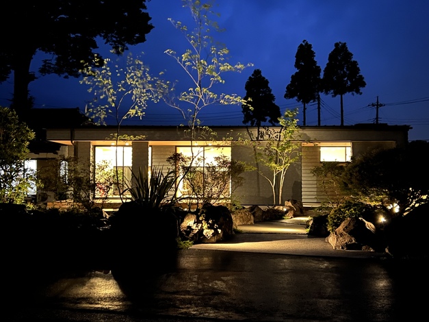 夜の庭園が美しくライトアップされた住宅の外観。落ち着いた風景に包まれた家は、静寂と自然を感じる場所である。