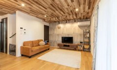 天井に木目調のパネルを使用したリビング。ゆったりとしたソファと広いラグがあり、居心地の良い空間を演出している。【ユースタイルハウス　上村建設】