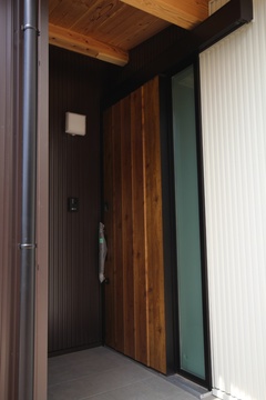 木目のドアが印象的な玄関。シンプルでありながら温かみのある雰囲気を醸し出し、訪れる人を優しく迎える。【明城】