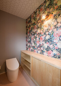 将来に備え、トイレもゆとりある広さに。華やかな花柄のクロスをはじめ、1階の各空間のクロスは奥さまがセレクトした。造作による収納カウンターは利便性も高い【ホームプラザ大東】