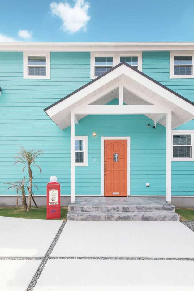 ブルー＆ホワイトにオレンジ色のドアがポップな玄関。かわいらしいポストとパームツリーがお出迎え