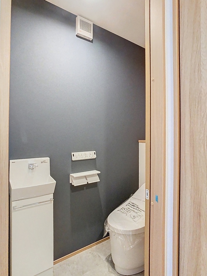 グレーのアクセントクロスを取り入れたトイレは、落ち着きのあるシンプルな仕上がり。手洗い器付きで使いやすく、清潔感のある空間にまとめています。