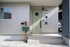 シンプルでモダンなデザインの玄関。緑色のドアが印象的で、周囲の白い壁とのコントラストが美しい。小さな窓があり、光が入りやすく明るい印象を持たせている。【ハレノイエ （中村土建）】