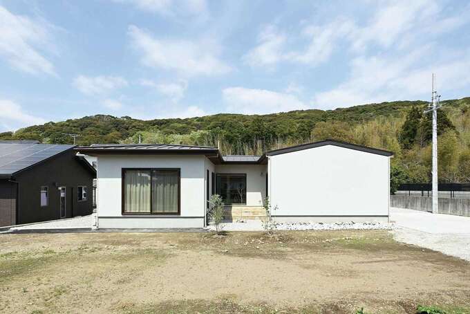 中庭を囲む「コ」の字型の平屋の外観。淡いグレーの塗り壁を外壁に用い、シンプルで上品な印象に。屋根の架け方を変えて個性を演出した