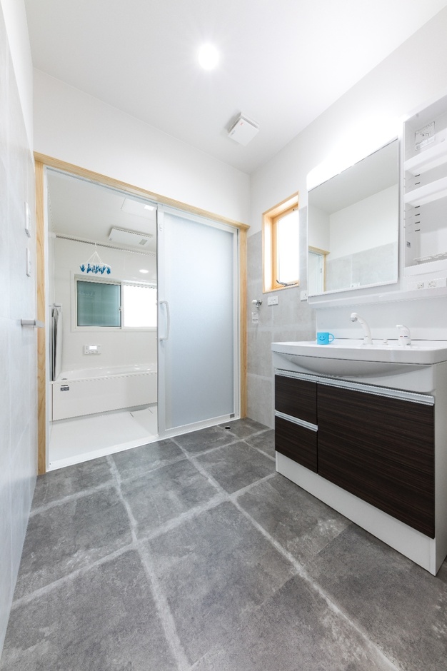 広々とした洗面脱衣スペース。清潔感のあるタイル床と壁には大きな鏡が設置され、洗面台も機能的で収納力が高い。