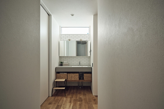 玄関のすぐ隣に設けた洗面スペースは、帰宅してすぐ手洗いができるよう配慮。カウンターには「サンワカンパニー」のモルタル調の素材を採用。３面鏡の上には明かり取りの窓を設けてある