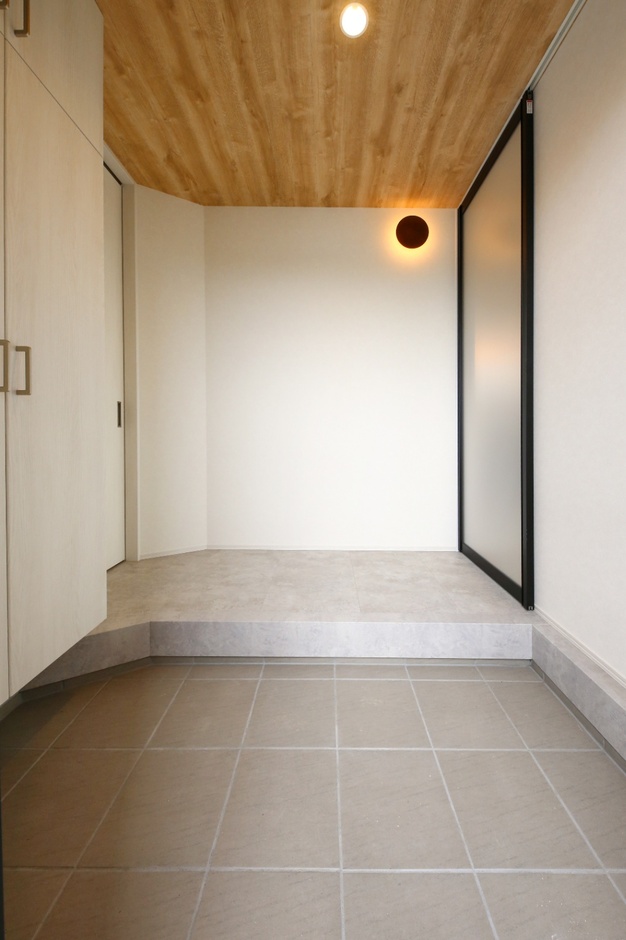 シンプルで落ち着いた雰囲気の玄関。木の天井と温かい照明が、訪れる人に穏やかで心地よい印象を与える。