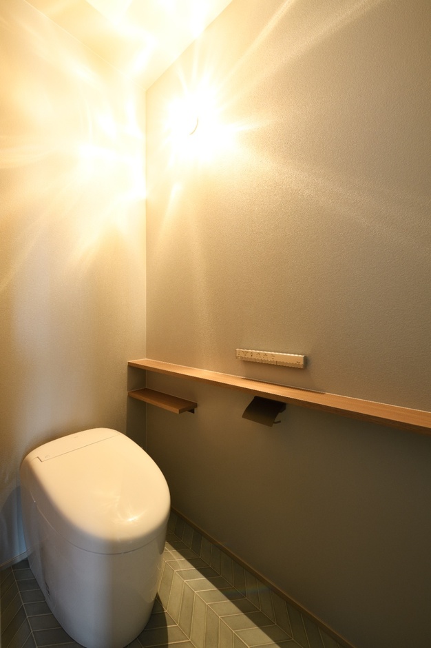 シンプルかつ機能的なトイレ空間。壁に取り付けられた木製の棚が温かみを演出し、落ち着ける空間を形成している。