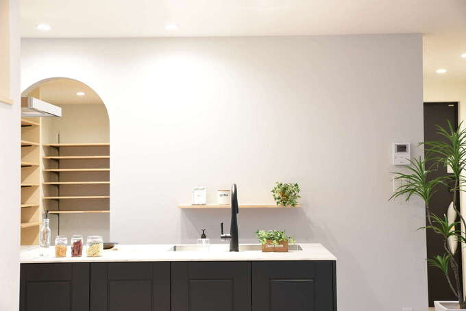 冷蔵庫や調理家電をバックヤードに収納して生活感を出さない。淡いグレーの壁は漆喰