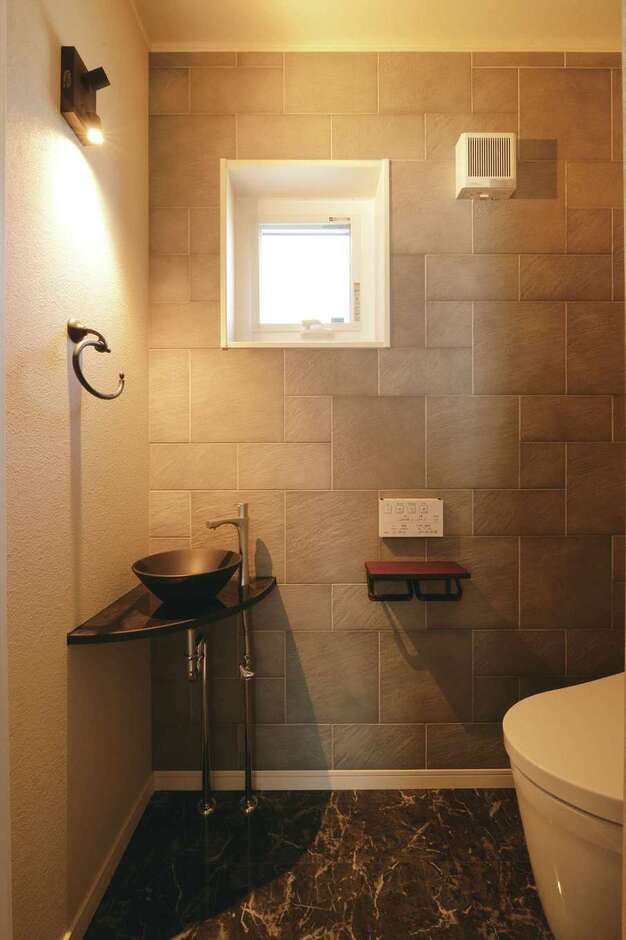 トイレは石目調のフロアタイルやコンクリート風の壁紙をベースに、洗面ボウルと照明を黒でまとめてインダストリアルな雰囲気にコーディネート