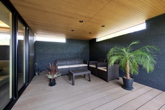 屋外にあるウッドデッキのスペース。ナチュラルな木材と植栽が調和し、リラックスできるアウトドアエリアを形成している。家具が配置され、ゆったりとした時間を過ごせる。
