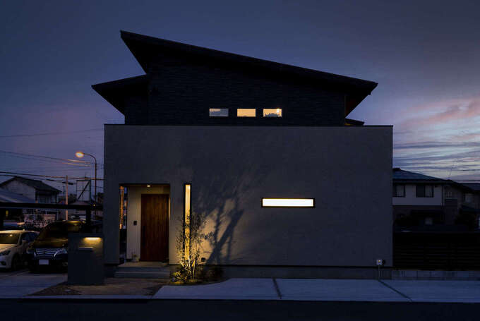 ボックス形状と片流れの屋根を組み合わせたフォルムが照明にほのかに照らされて、夜の闇に浮き立つ外観。外壁はサイディングと塗り壁、レッドシダー張りを組み合わせて、表情ゆたかに仕上げてある