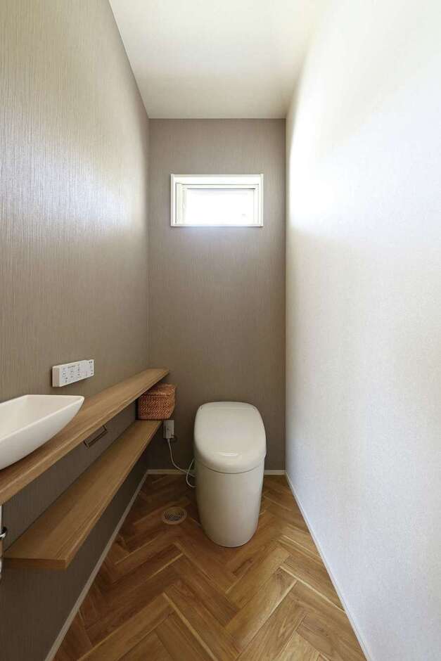 ヘリンボーン柄の床とグレーの壁が調和したトイレは手洗いカウンター付き