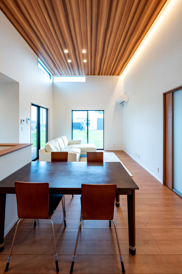 開放感あふれるLDK。高い天井と大きな窓が明るさを最大限に引き出している。木目調の天井が温かみを加えている。