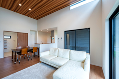 白いソファとモダンなインテリアが配置されたLDK。天井の木目が温かみを感じさせ、広々とした空間を演出している。大きな窓からの自然光が心地よい。