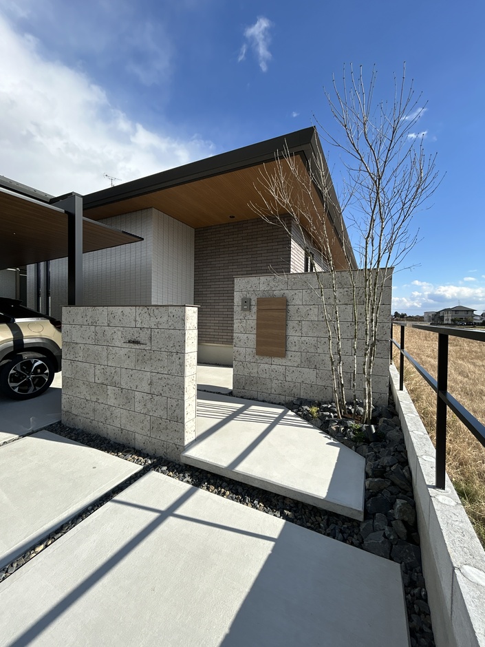 モダンなデザインの外観で、大きな軒が特徴的な建物。エントランスの石壁と周囲の開放感ある景色が調和している。