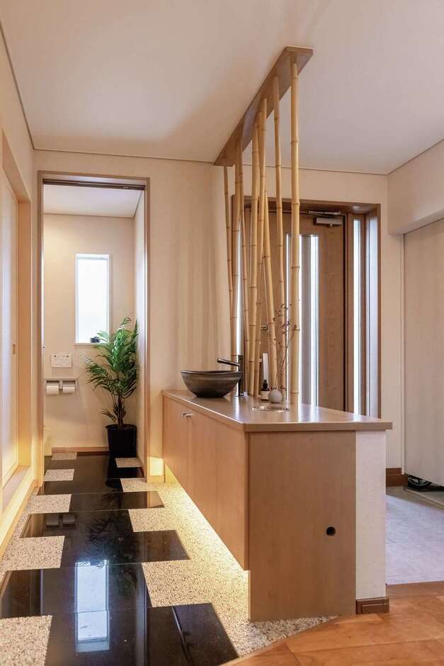 和とモダンが共鳴する玄関ホール。リビングを通らずに、和室からトイレにアクセスできるのでゲストも安心。黒御影石と間接照明のアプローチが高級感を演出