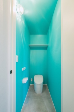 鮮やかなターコイズブルーの壁で彩られたモダンなトイレ空間である。シンプルなデザインにより落ち着いた雰囲気を演出し、洗練された印象を与える。【オオトリ建設】