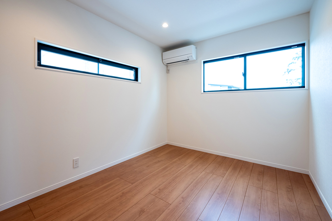 白と木目が調和するシンプルな居室。大きな窓から自然光が差し込み、明るく開放的な空間が広がる。エアコンが設置され、快適に過ごせる設計となっている。