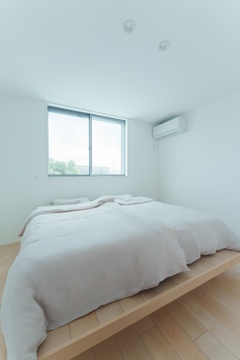 シンプルでモダンな寝室。大きな窓からは明るい自然光が差し込み、部屋全体に清潔感を与えている。エアコンも設置され、快適な環境が整えられている。【オオトリ建設】